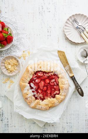 Galette de fraises. Tarte aux fraises maison avec du sucre en poudre de fraises fraîches et des flocons d'amandes pour la partie de thé d'été sur fond de bois clair. T Banque D'Images