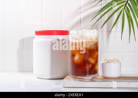 Verre de boisson au café latte collagène avec de la poudre de collagène dans un pot et une cuillère, sur une table de cuisine blanche. Supplément naturel pour la beauté, la santé de la peau, les os, Banque D'Images