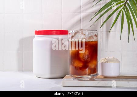 Verre de boisson au café latte collagène avec de la poudre de collagène dans un pot et une cuillère, sur une table de cuisine blanche. Supplément naturel pour la beauté, la santé de la peau, les os, Banque D'Images