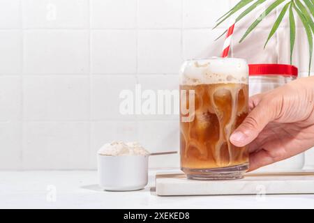 Verre de boisson au café latte collagène avec de la poudre de collagène dans un pot et une cuillère, sur une table de cuisine blanche. Supplément naturel pour la beauté, la santé de la peau, les os, Banque D'Images