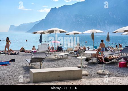Nago Torbole, Lac de Garde, Italie - 27 juin 2024: les touristes profitent de la journée ensoleillée sur la plage de Torbole Spiaggia Lungolago à Torbole sur le lac de Garde en transats avec parasols *** Touristen genießen den sonnigen Tag an dem Strand à Torbole Spiaggia Lungolago à Torbole am Gardasee à Liegestühlen mit Sonnenschirmen Banque D'Images