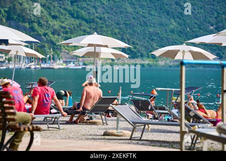 Nago Torbole, Lac de Garde, Italie - 27 juin 2024: les touristes profitent de la journée ensoleillée sur la plage de Torbole Spiaggia Lungolago à Torbole sur le lac de Garde en transats avec parasols *** Touristen genießen den sonnigen Tag an dem Strand à Torbole Spiaggia Lungolago à Torbole am Gardasee à Liegestühlen mit Sonnenschirmen Banque D'Images