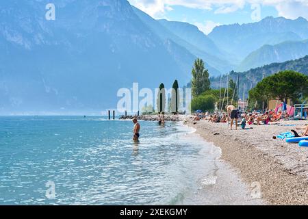 Nago Torbole, Lac de Garde, Italie - 27 juin 2024 : les touristes apprécient la journée ensoleillée sur la plage de Torbole Spiaggia Lungolago sur le Lac de Garde et bronzer et nager *** Touristen genießen den sonnigen Tag an dem Strand in Torbole Spiaggia Lungolago am Gardasee und lassen sich sonnen und baden Banque D'Images