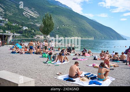 Nago Torbole, Lac de Garde, Italie - 27 juin 2024 : les touristes apprécient la journée ensoleillée sur la plage de Torbole Spiaggia Lungolago sur le Lac de Garde et bronzer et nager *** Touristen genießen den sonnigen Tag an dem Strand in Torbole Spiaggia Lungolago am Gardasee und lassen sich sonnen und baden Banque D'Images