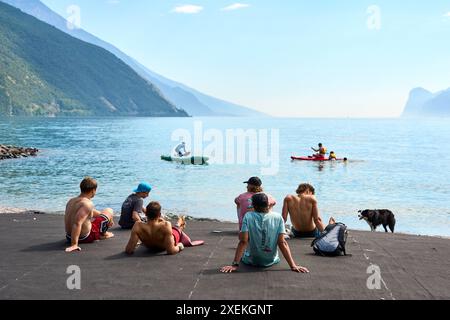 Nago Torbole, Lac de Garde, Italie - 27 juin 2024 : les touristes apprécient la journée ensoleillée sur la plage de Torbole Spiaggia Lungolago sur le Lac de Garde et bronzer et nager *** Touristen genießen den sonnigen Tag an dem Strand in Torbole Spiaggia Lungolago am Gardasee und lassen sich sonnen und baden Banque D'Images