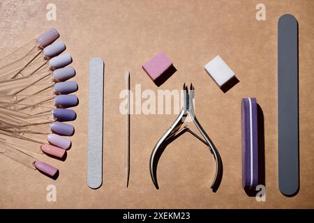 Plan plat d'outils de manucure ensemble de limes à ongles droites, pousseur de cuticule en bois, blocs tampons et bâtons d'échantillon d'ongles tout en couleur lavande sur fond beige, espace de copie Banque D'Images