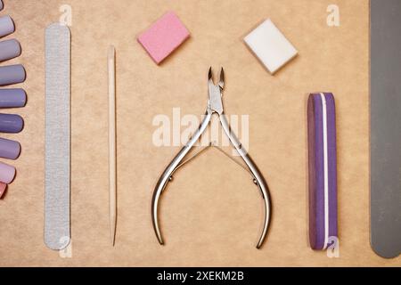 Plan de pose plate d'outils de base pour le soin des ongles sur fond beige. Manucure à la maison ensemble de limes à ongles, blocs tampons, bâton orange et pinces à cuticules, concept de soins des mains Banque D'Images