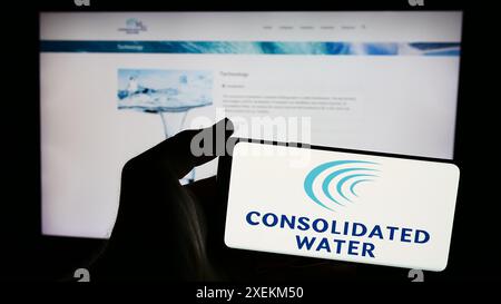 Personne tenant un smartphone avec le logo de la société de dessalement d'eau de mer Consolidated Water Co. Ltd en face du site Web. Concentrez-vous sur l'affichage du téléphone. Banque D'Images