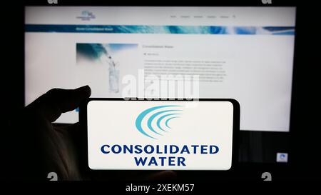 Personne tenant le téléphone portable avec le logo de la société de dessalement d'eau de mer Consolidated Water Co. Ltd devant la page Web. Concentrez-vous sur l'affichage du téléphone. Banque D'Images