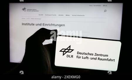 Personne tenant un téléphone portable avec le logo de Deutsches Zentrum für Luft- und Raumfahrt e.V. (DLR) devant la page web. Concentrez-vous sur l'affichage du téléphone. Banque D'Images