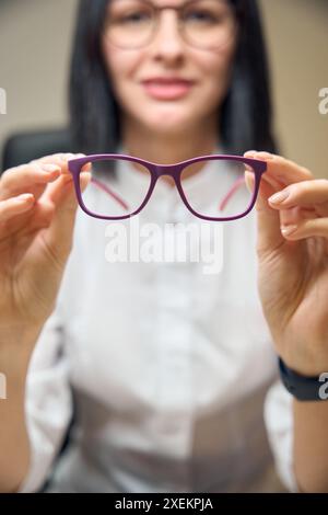 Brunette tient des verres avec des montures lilas dans ses mains Banque D'Images