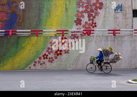 Vendeur de fleurs vendeur de fleurs à vélo par mur de mosaïque à Hanoi, Ha Noi, Nord Vietnam, Asie en juin Banque D'Images