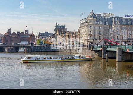 Amsterdam, pays-Bas - 14 mai 2018 : long bateau canal Cruises devant l'hôtel Victoria au Sunny Spring Day. Banque D'Images