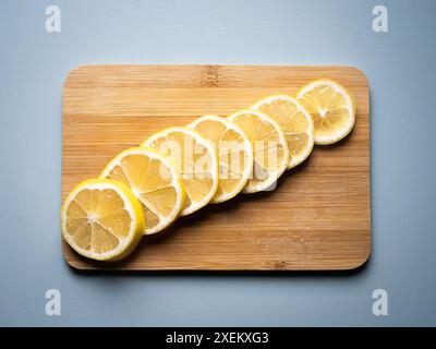 Un citron tranché disposé sur une planche à découper en bois de bambou sur une table bleu clair, éclairage doux, espace copie, pas de personnes Banque D'Images