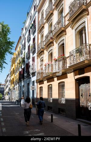 Les piétons marchent le long d'une rue devant un immeuble résidentiel avec balcons décoratifs par une journée ensoleillée à Chueca, Madrid ; Madrid, Espagne Banque D'Images