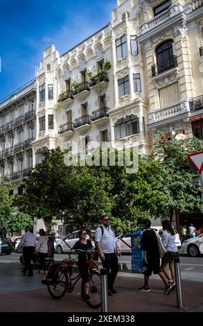 Scène de rue avec des piétons et des cyclistes, des véhicules garés et un bâtiment résidentiel orné sur une journée ensoleillée à Madrid ; Madrid, Espagne Banque D'Images