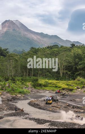 Les véhicules utilitaires sport courent dans l'eau et la boue avec le sommet du mont Merapi en arrière-plan dans le centre de Java, en Indonésie Banque D'Images