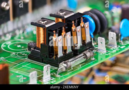 Composants électroniques comme relais électromagnétiques ou fusible électrique en verre sur PCB vert. Gros plan sur deux commutateurs électromécaniques avec bobine sur carte de circuit imprimé. Banque D'Images