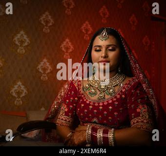 Une mariée indienne en tenue traditionnelle, ornée de bijoux complexes assis les yeux fermés dans une pièce avec lumière rouge Banque D'Images