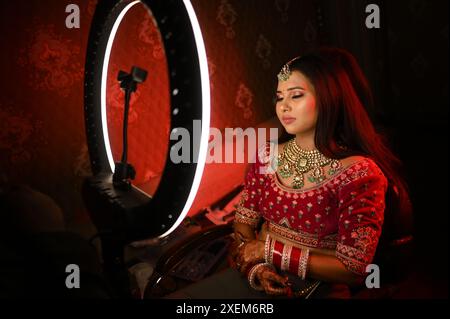 Une mariée indienne en tenue traditionnelle, ornée de bijoux complexes assis les yeux fermés devant un anneau lumineux lumineux Banque D'Images