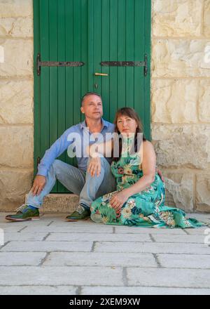 Portrait d'un beau couple d'âge moyen devant une porte en bois vert. L'homme regarde loin et la femme regarde la caméra. Banque D'Images