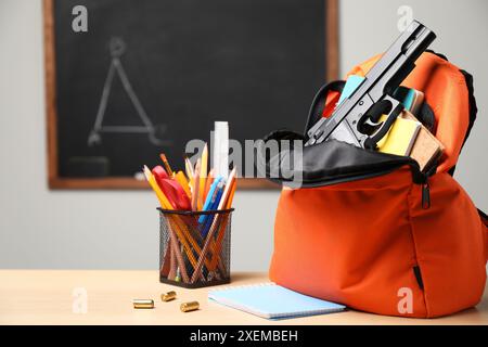 Arme à feu, balles et papeterie scolaire sur une table en bois près du tableau noir à l'intérieur, espace pour le texte Banque D'Images