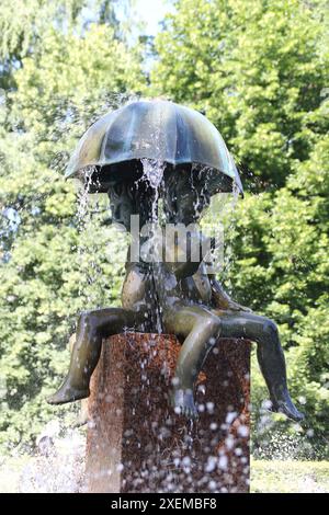 Enfants & enfants sous un parapluie sous la pluie - la fontaine dans le parc Kanuti, Tallinn, Estonie Banque D'Images