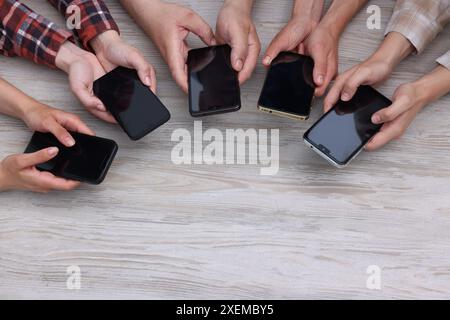 Personnes tenant des smartphones avec des écrans blancs à la table en bois, vue de dessus. Maquette pour le design Banque D'Images