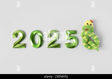 Jouet tricoté serpent vert rayé et numéros verts. Le symbole de l'année 2025 sur fond gris. Banque D'Images