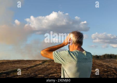 Gros plan d'un homme qui est sur le dos et qui a les mains sur la tête regardant son champ brûlé après le feu. Il y a de la fumée en arrière-plan de l'image. Banque D'Images