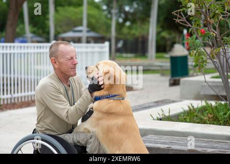 Homme en fauteuil roulant montrant de l'affection pour son chien d'assistance dans un parc de la ville, l'homme et le chien se regardant face à face Banque D'Images