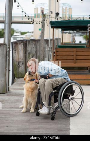 Homme en fauteuil roulant montrant de l'affection pour son chien d'assistance tout en passant du temps à l'extérieur ; Boynton Beach, Floride, États-Unis d'Amérique Banque D'Images