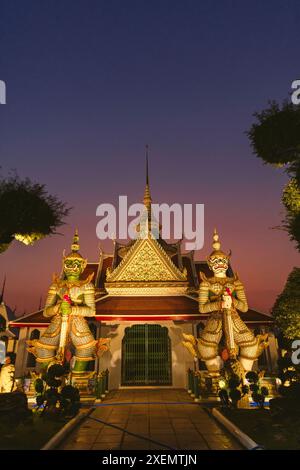 Wat Arun Ratchawararam Ratchawaramahawihan avec statues du gardien Yaksha à l'entrée de la salle d'ordination, illuminées au crépuscule Banque D'Images