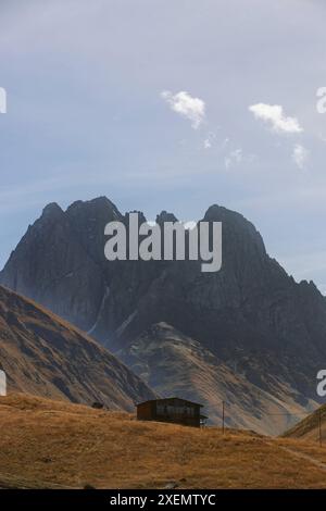 Les sommets escarpés des montagnes se dressent au-dessus d'une maison dans une vallée dans le parc national de Kazbegi ; Géorgie Banque D'Images