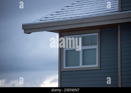 Gros plan d'une maison moderne avec un toit enneigé et de grandes fenêtres contre un ciel nuageux. Banque D'Images