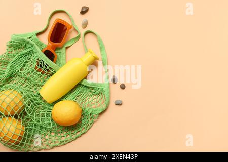 Bouteille de crème solaire, sac à ficelle avec des citrons et des lunettes de soleil sur fond orange Banque D'Images