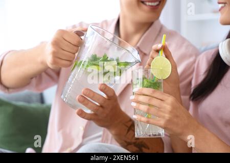 Heureux jeune couple versant du mojito savoureux dans le verre à la maison, gros plan Banque D'Images