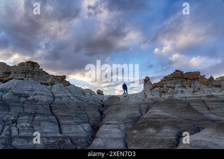 Vue en angle bas d'un homme debout au sommet de formations rocheuses accidentées sous un grand ciel nuageux dans Valley of Dreams, Nouveau-Mexique, États-Unis Banque D'Images