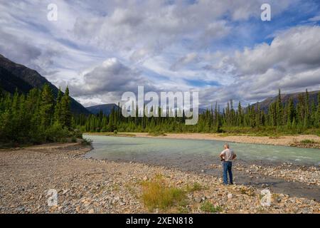 Vue prise de derrière d'un homme debout le long de la rivière Wheaton profitant de la vue par une belle journée d'été ; Whitehorse, Yukon, Canada Banque D'Images