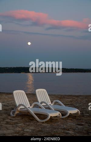 Chaises longues le long du front de mer au crépuscule à Novigrad, Croatie ; Novigrad, comté d'Istrie, Croatie Banque D'Images