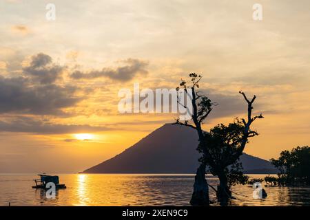 Le coucher de soleil brille de lumière dorée sur l'île silhouette et l'océan tranquille dans le parc marin national de Bunaken en Indonésie ; Bunaken, Sulawesi du Nord, Indonésie Banque D'Images