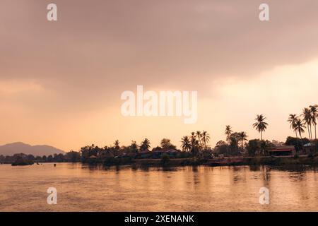 Reflets de coucher de soleil le long du fleuve Mékong avec des palmiers bordant le rivage au Laos ; Don Khon, Province de Champasak, Laos Banque D'Images