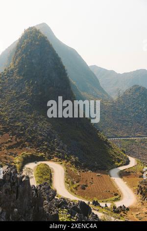 Route avec virages inversés serpentant à travers une vallée avec des montagnes culminantes dans la campagne du Vietnam Banque D'Images