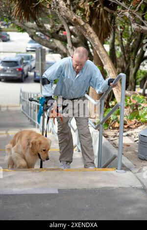 Homme paraplégique grimpe les marches avec une main courante, une béquille d'avant-bras et un chien d'assistance ; Boynton Beach, Floride, États-Unis d'Amérique Banque D'Images