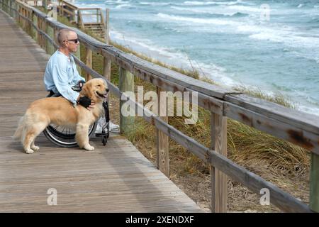 Homme paraplégique en fauteuil roulant avec chien d'assistance profite de la vue sur l'océan depuis une promenade ; Boynton Beach, Floride, États-Unis d'Amérique Banque D'Images