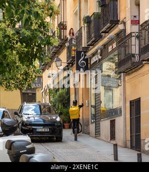 06.19.2024, Madrid, Espagne : un livreur Glovo sur un vélo parlant à une cliente sur un balcon dans une rue de Madrid Banque D'Images