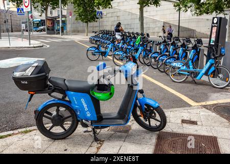 06.19.2024, Madrid, Espagne : Cooltra location scooter bleu avec des casques suspendus de guidon et un couple louant vélo à partir d'une station d'accueil BiciMAD Behi Banque D'Images