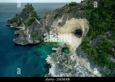 Plage de sable blanc avec arche naturelle le long d'une côte accidentée dans la mer des Moluques, dans le Sulawesi central, Indonésie Banque D'Images