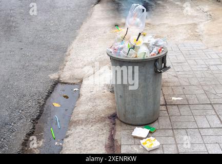 Vieille poubelle en plastique gris sale avec beaucoup de déchets à l'intérieur est sur le côté de la route dans la ville. Banque D'Images