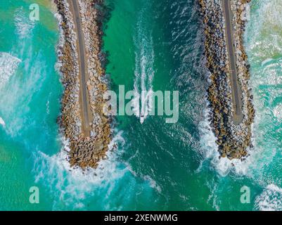 Vue aérienne d'un petit bateau se dirigeant vers la mer entre des murs brise-lames à Narooma sur la côte sud de la Nouvelle-Galles du Sud, Australie. Banque D'Images